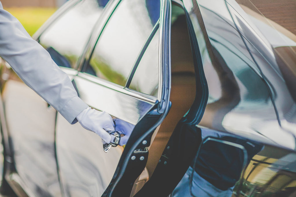 A man in a suit is holding the door handle of a car